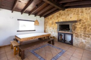 Salón con chimenea y detalle de mesa con bancos frente cristalera de la villa individual de la calle central de Lajares, Fuerteventura