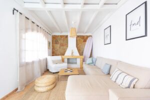 Salón y detalle de sofas y chimenea al fondo de color blanco de la villa de la calle central de Lajares, Fueteventura