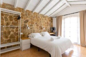 Dormitorio con detalle de pared de cabecera de piedra rústica de la Villa en la calle central de Lajares, Fueteventura