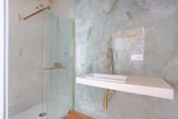 Baño con mampara de ducha y grifos en color oro de los apartamentos de planta alta del edificio de 4 apartamentos en El Cotillo