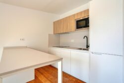 Cocina, suelo de tarima de madera y mobiliario blanco y madera clara de los apartamentos de planta alta del edificio de 4 apartamentos en El Cotillo